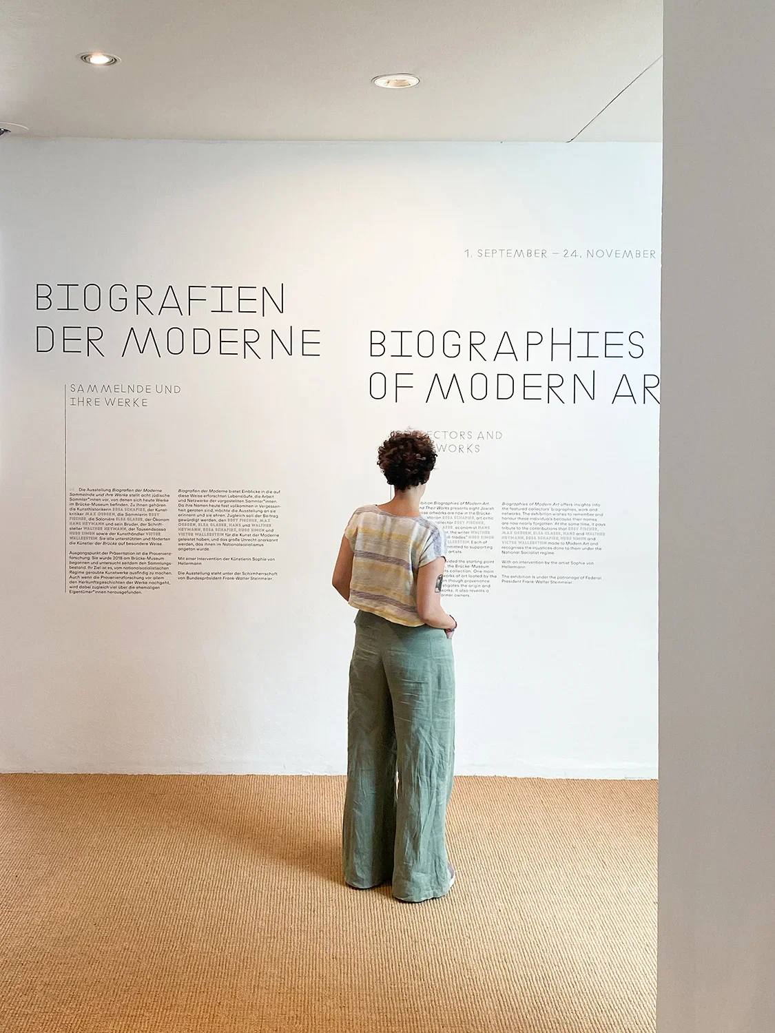 Person standing in front of the bilingual introduction wall “Biografien der Moderne / Biographies of Modern Art”.