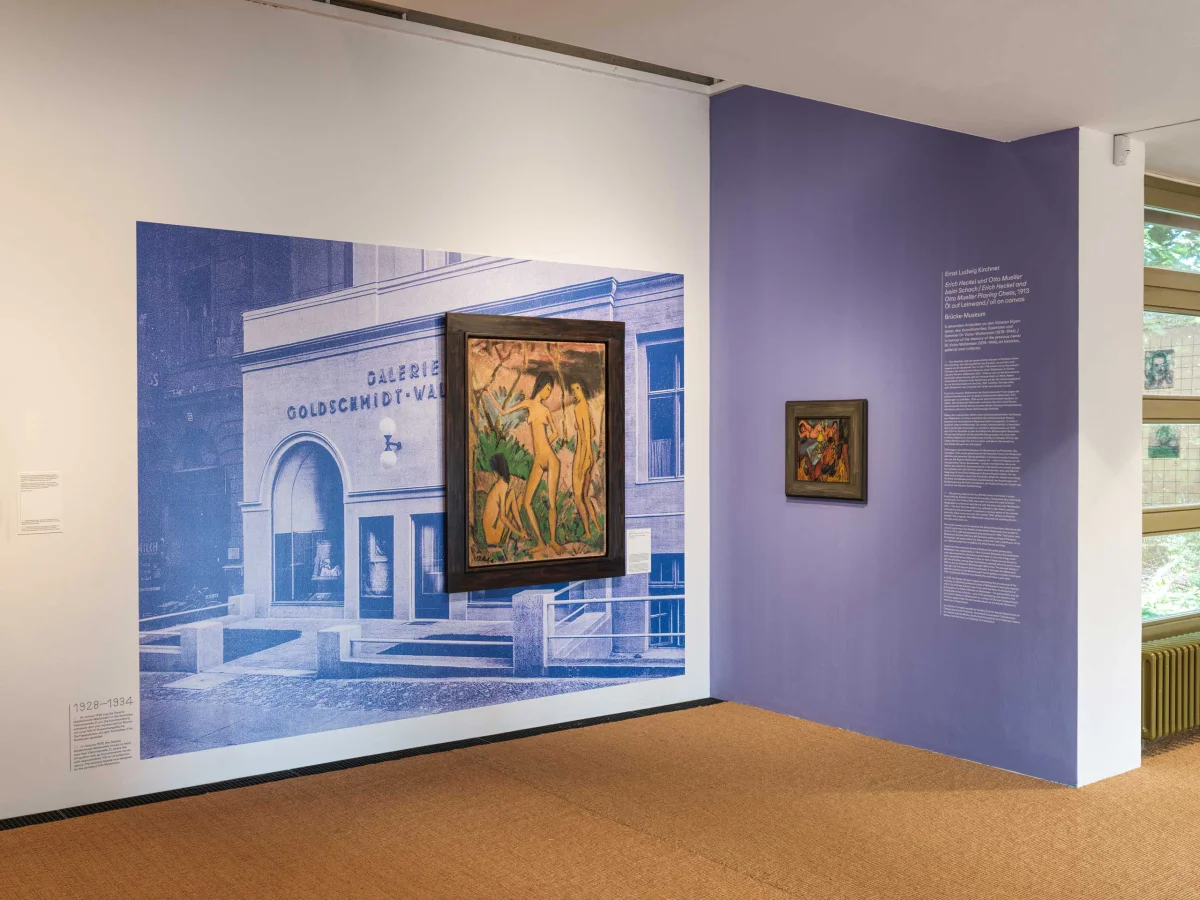 Framed painting in front of a blue historical gallery photograph beside a purple text wall.