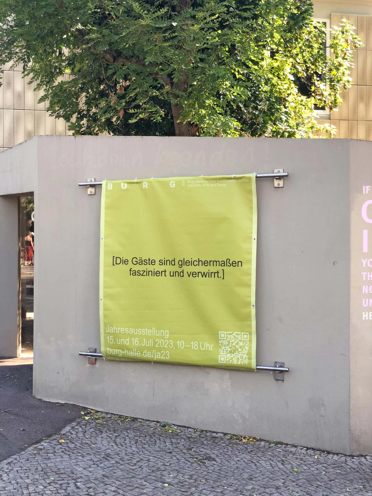 Yellow-green exhibition banner on a wall reading, in German: “The guests are equally fascinated and confused.”