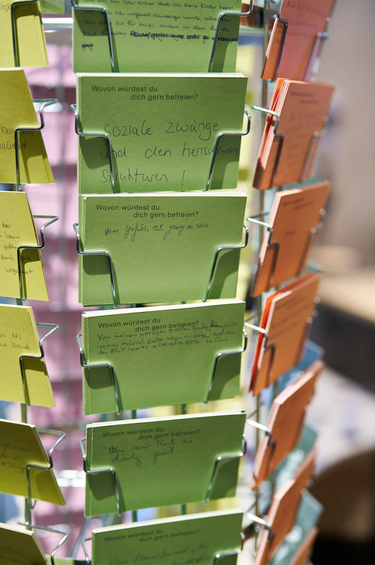 Nahaufnahme eines Drahtständers mit grünen, rosa und orangefarbenen Antwortkarten, teilweise mit handschriftlichen Einträgen.