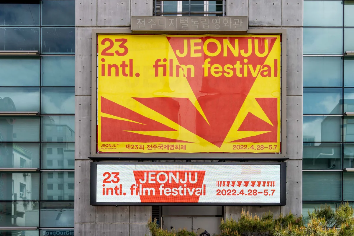 Rot-gelbe JEONJU-Festivalbanner an einer Glas- und Betonfassade, mit dem Veranstaltungszeitraum 28. April bis 7. Mai 2022.