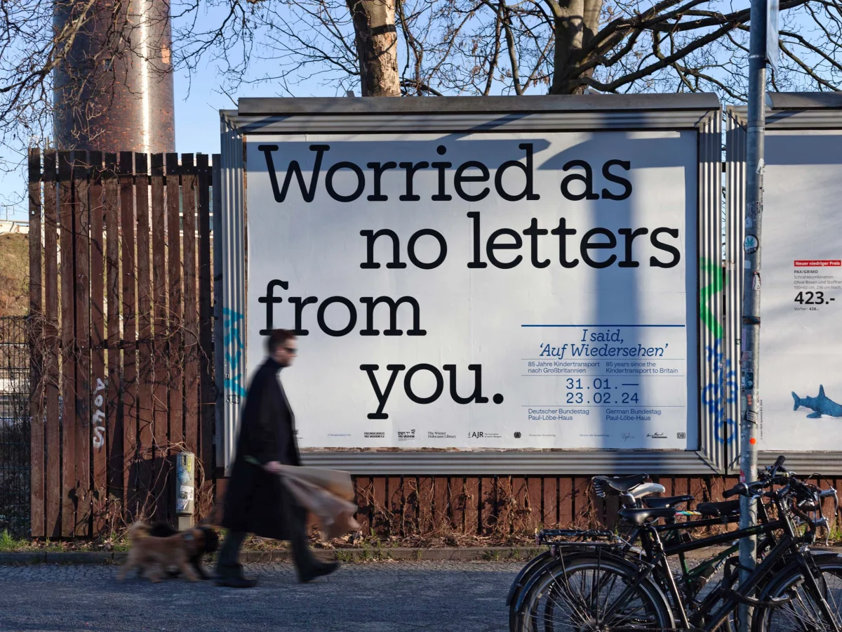 Street-mounted poster reading “Worried as no letters from you.”, with a passer-by and parked bicycles in front.