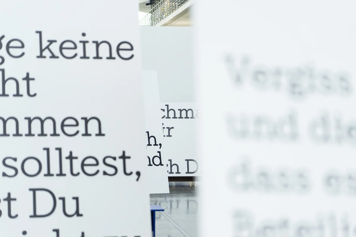 Close-up of black letter quotations on staggered white exhibition panels, with blurred foreground and background.
