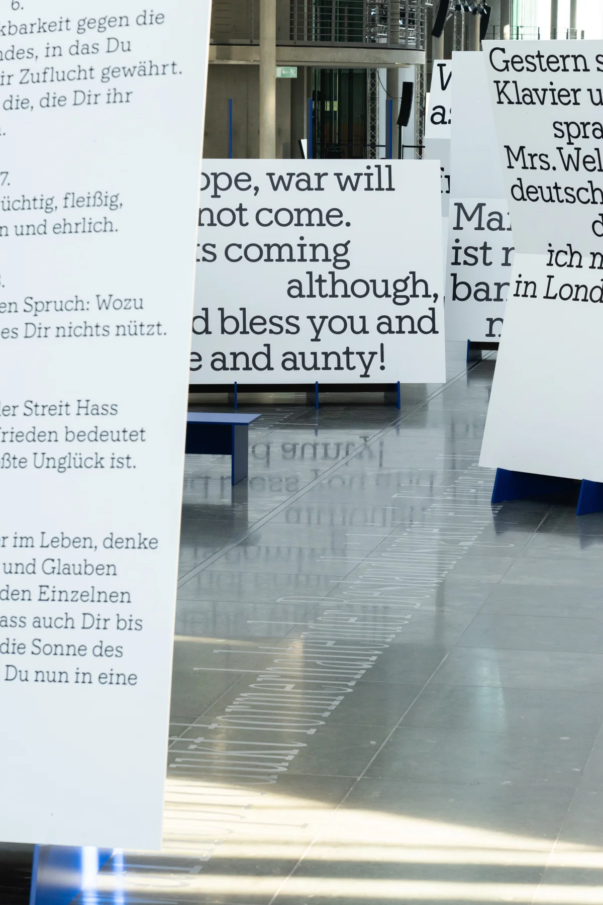 View between white exhibition panels carrying oversized German and English letter quotations.