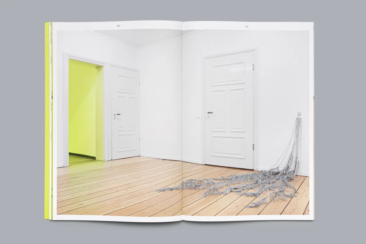 Doppelseitige Ausstellungsfotografie mit weißen Türen, gelbgrünem Durchgang und einer Metallinstallation auf dem Holzboden.