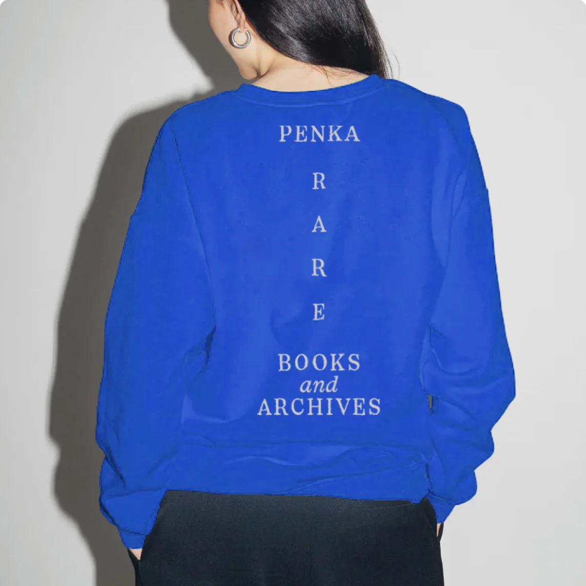 Rückenansicht einer Person im blauen Sweatshirt mit heller, senkrecht angeordneter PENKA-Wortmarke.