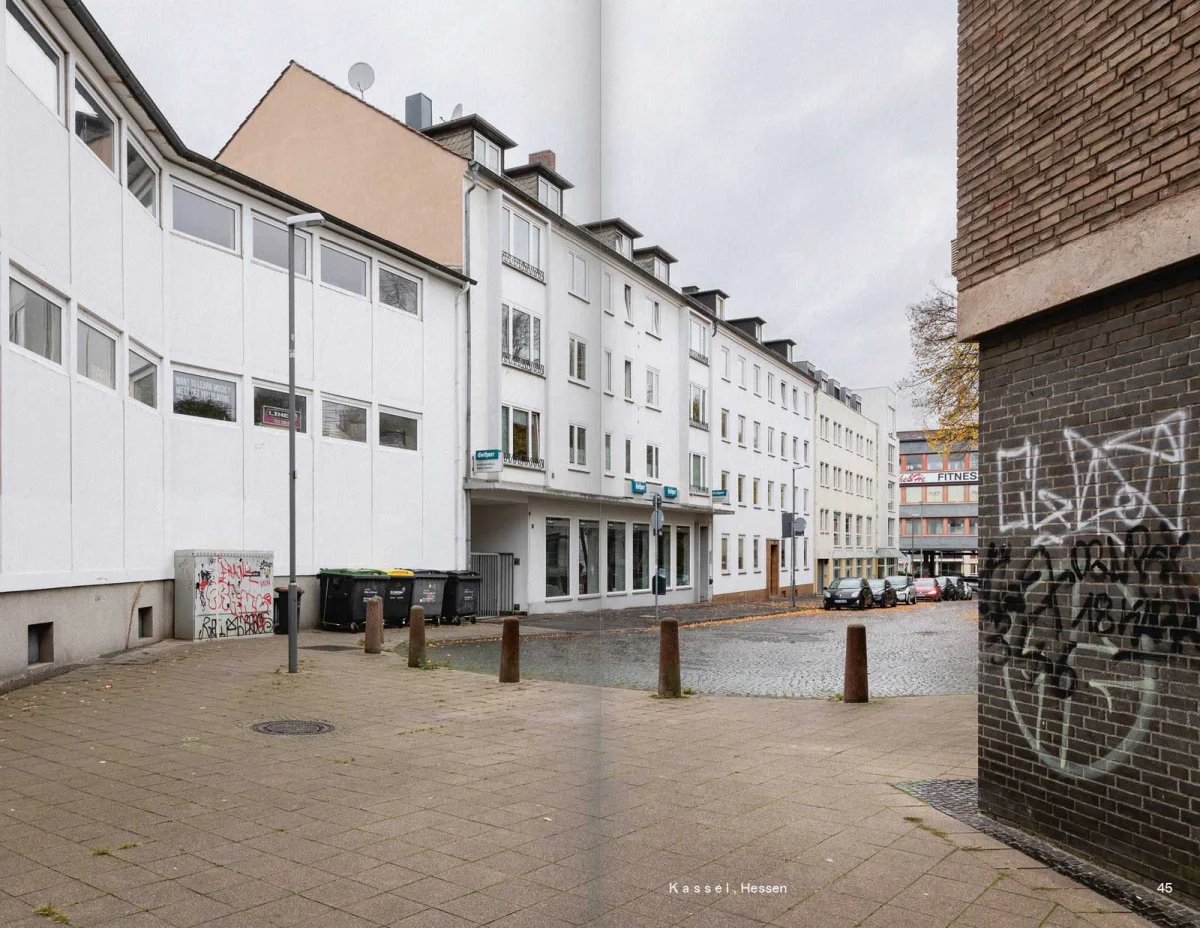 Full-spread contemporary courtyard photograph with residential buildings, bins and a graffiti-covered wall.