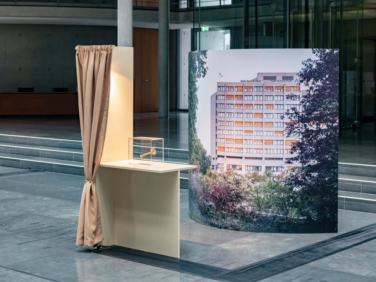Small display case beside a beige curtain, with a large photograph of a multi-storey building behind it.