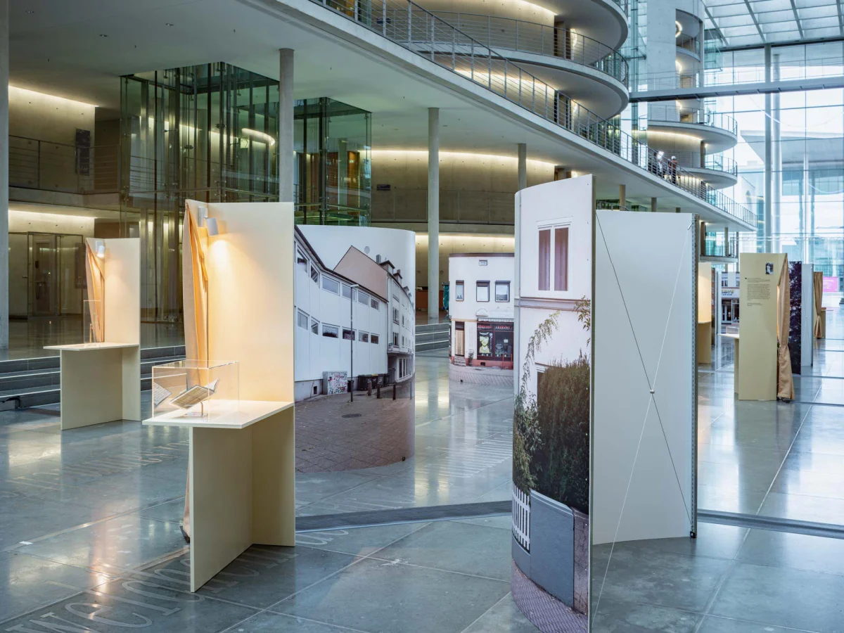 Exhibition view with illuminated object cases and curved panels displaying contemporary building photographs.