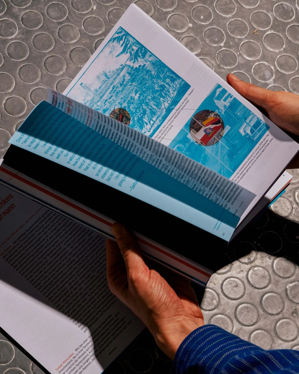 Hands turning a “Specology” spread featuring turquoise-toned images.