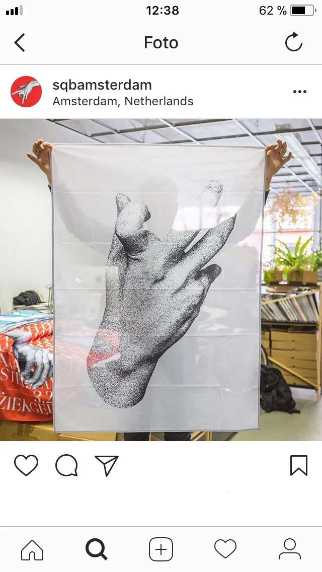 Instagram post showing a white fabric banner held up with a large black-and-white hand image.