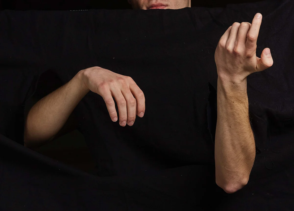 Two hands against black fabric, one hanging loosely and the other raised with curved fingers.