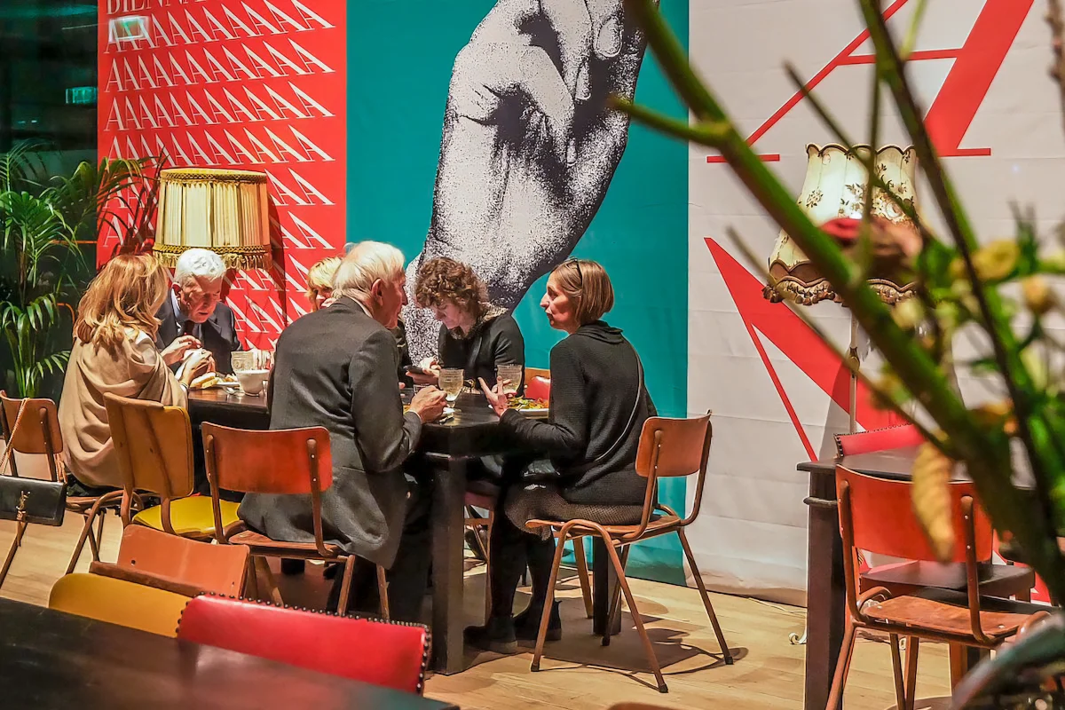Festival visitors seated at a table in front of large posters with hand imagery and expressive typography.