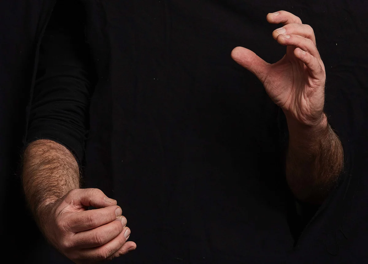 Close-up of two hands against black fabric, forming different fingering and playing gestures.