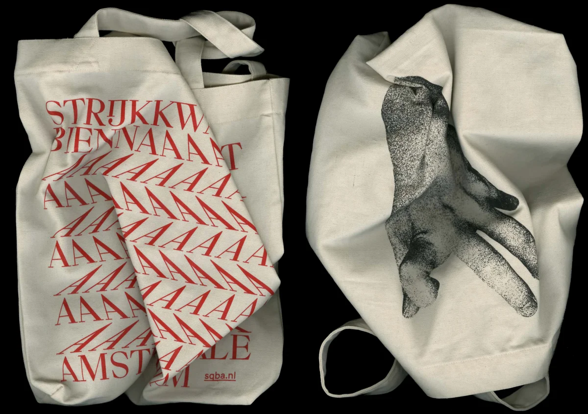 Two cream-coloured tote bags, one printed with red Biennale typography and the other with a black hand image.