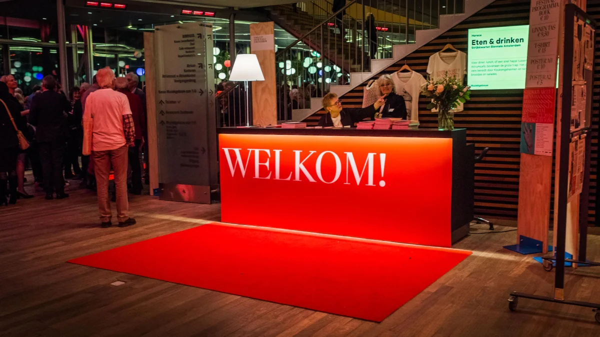 Red reception counter with white “Welkom!” lettering and a red carpet in the festival foyer.