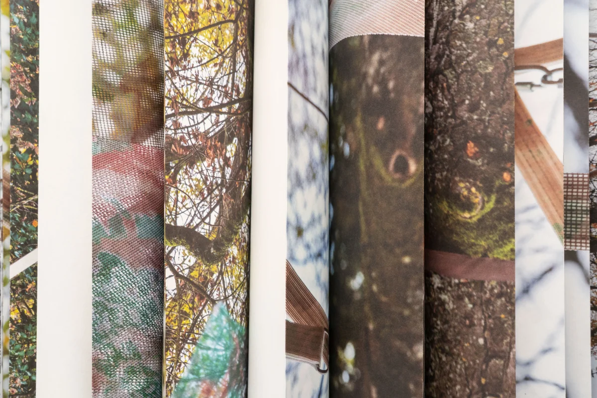 Close-up of folded book pages forming wavy strips that layer photographs of tree trunks, branches and patterned installation surfaces.