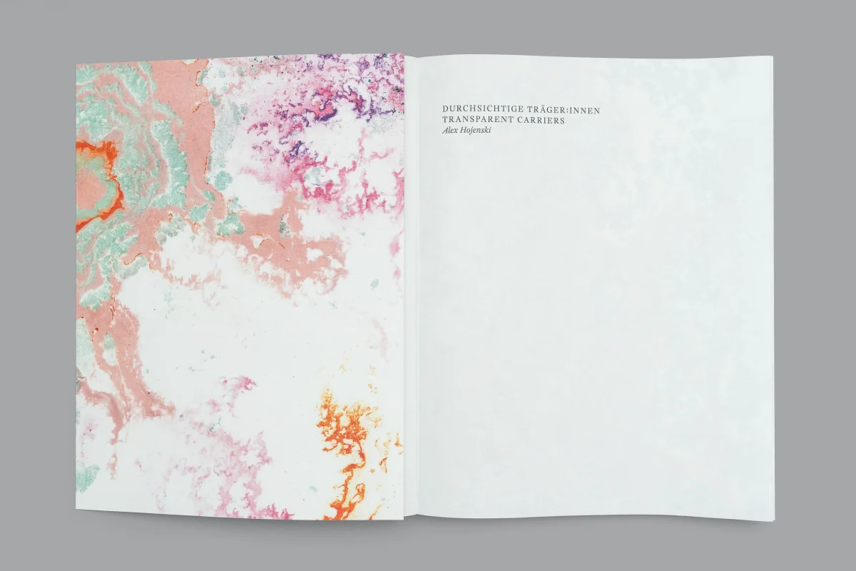 Open book with a pink and green patterned left page and a white title page for “Durchsichtige Träger*innen / Transparent Carriers”.
