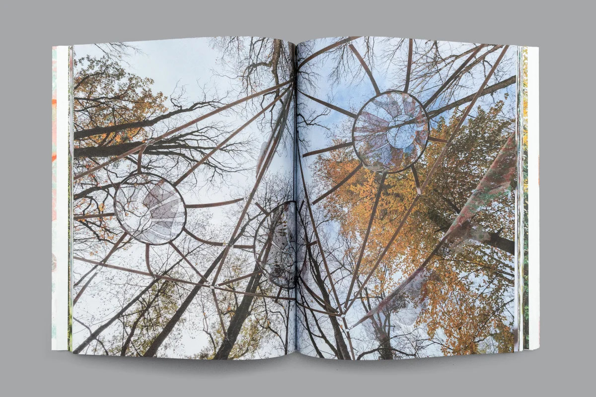 Book spread showing a radial steel structure among bare branches and autumn leaves against a blue sky.
