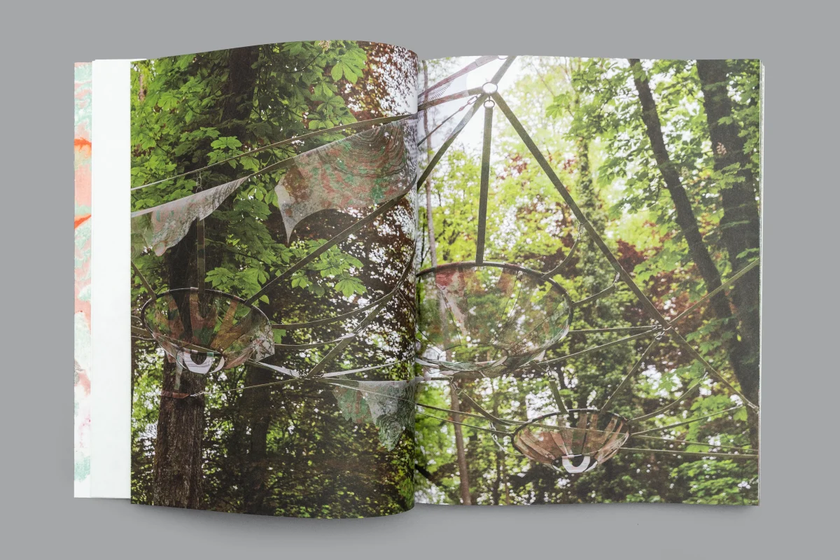 Photographic book spread looking into treetops where steel struts and cables support translucent patterned panels.